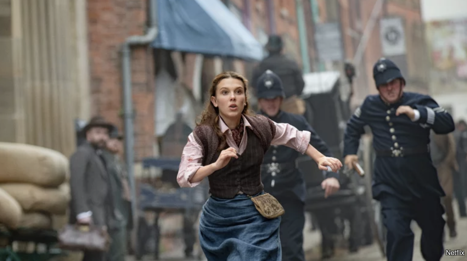 Promotional image of Enola Holmes 2 where Enola is chased by police officers; Netflix credit in bottom right-hand corner